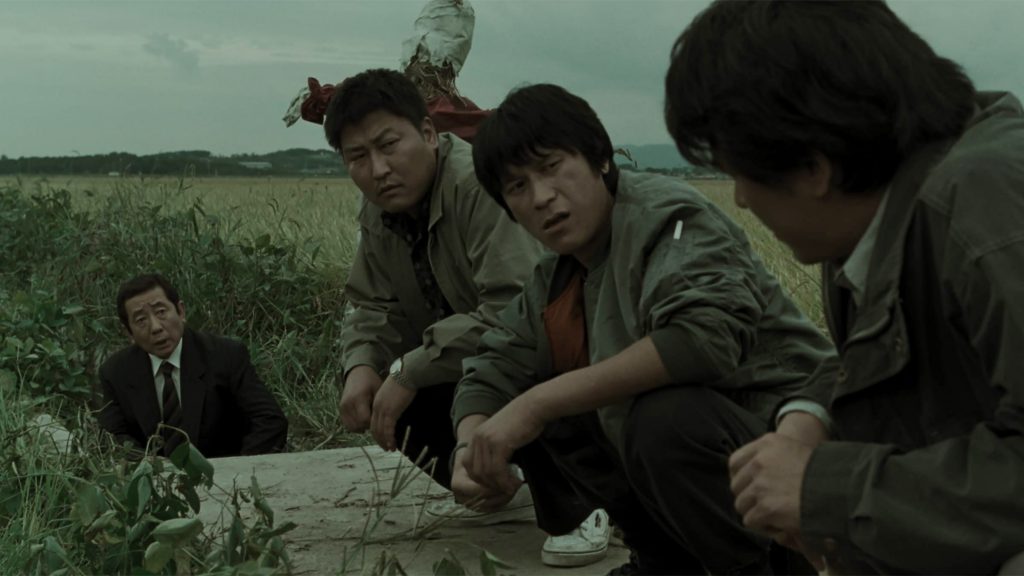 Still from "Memories of Murder" featuring four man crouching in a field