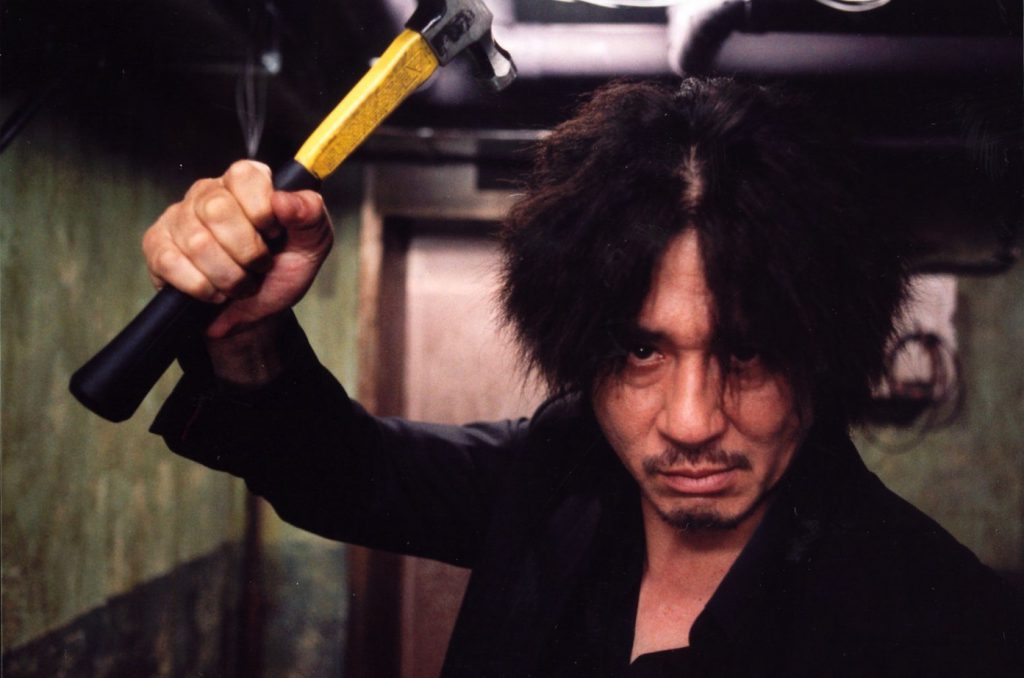 Still from "Oldboy" featuring the main character looking disheveled and wielding a hammer