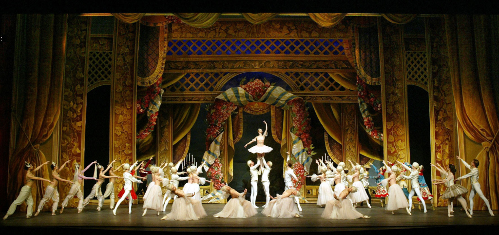 A still from "The Nutcracker" featuring the cast directing attention to the lead ballerina, who is being held up by two men