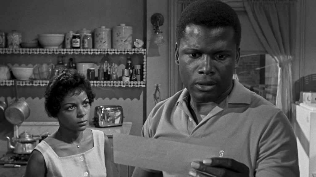 Still from "A Raisin in the Sun" featuring a woman looking at a man who is reading a letter with a concerned expression