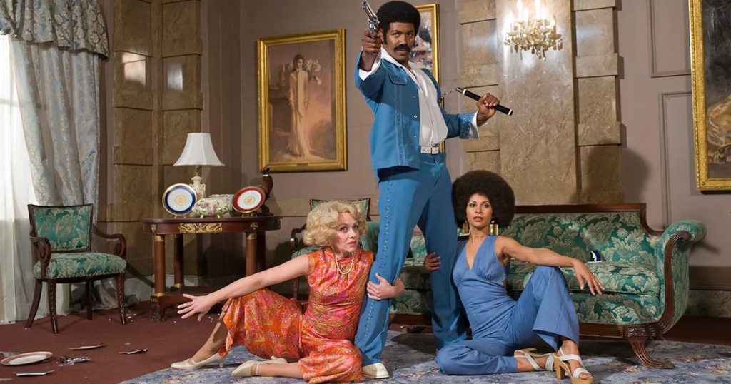 Still from "Black Dynamite" featuring a man pointing a gun while two women hold onto his legs