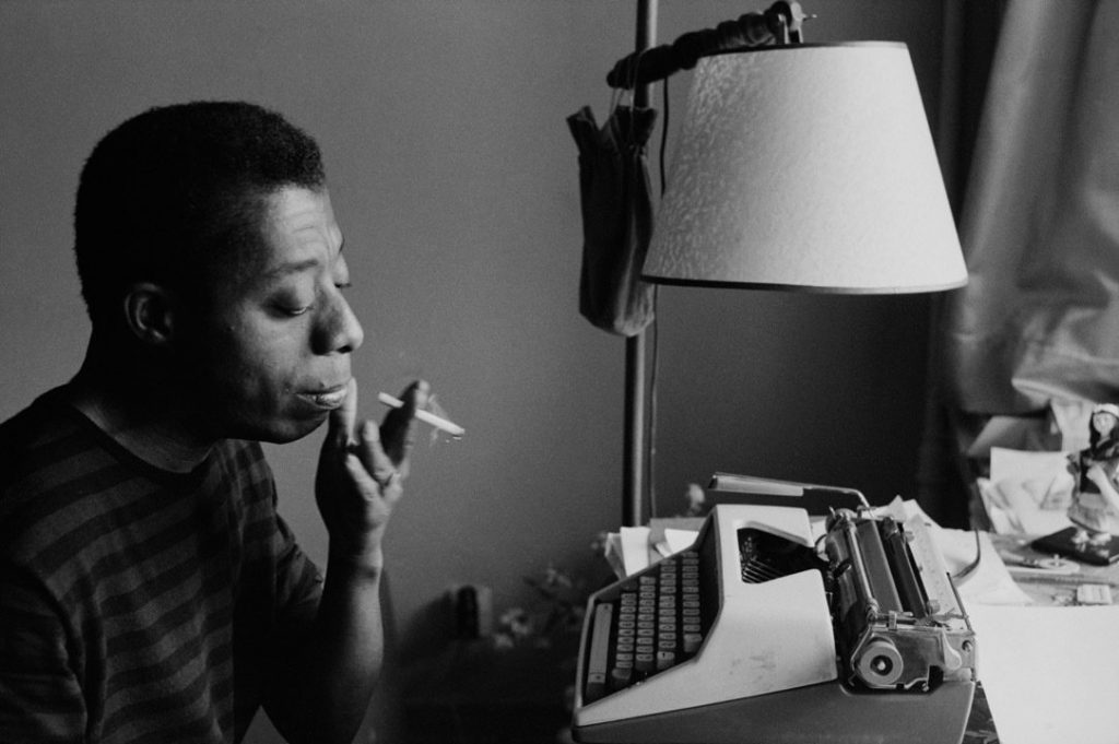 Still from "I Am Not Your Negro" featuring James Baldwin smoking while sitting at a typewriter