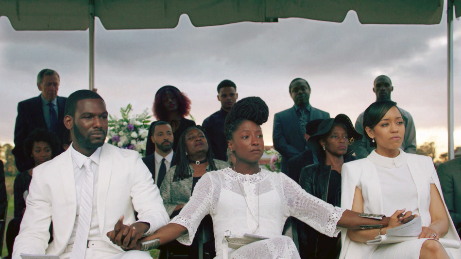 Still from "Queen Sugar" featuring three individuals dressed in white holding hands at a funeral