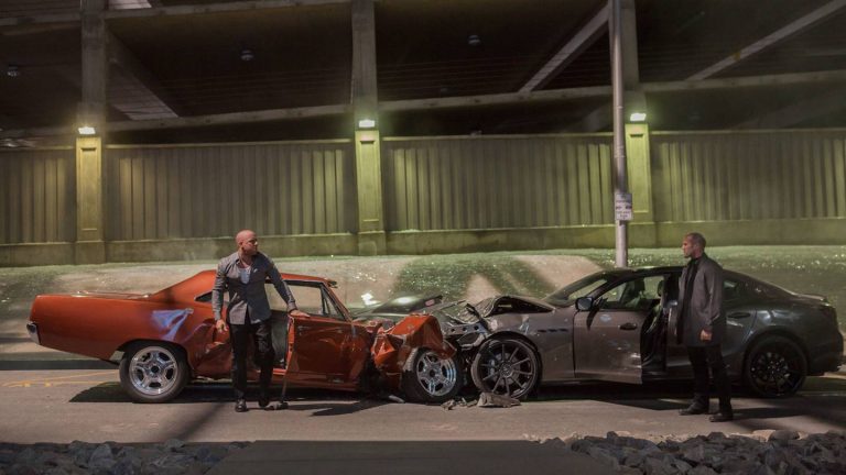 Still from "Furious 7" featuring two men standing beside two crashed sports cars