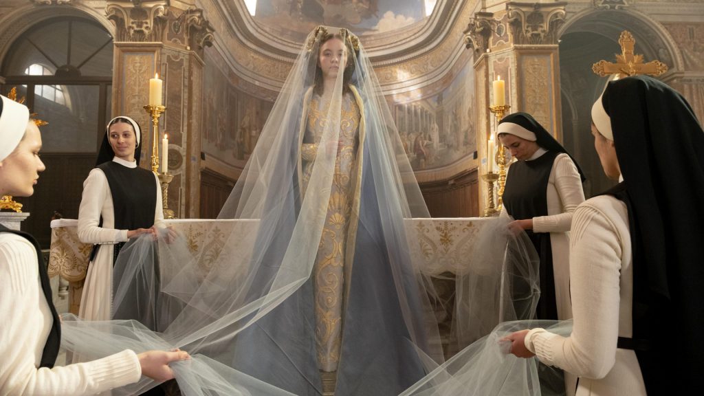 Still from "Immaculate" featuring nuns holding the veil of a woman standing at an altar