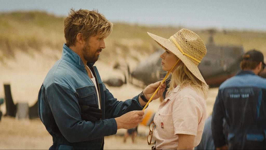 Still from "The Fall Guy" featuring a man tightening the strap of a woman's sun hat