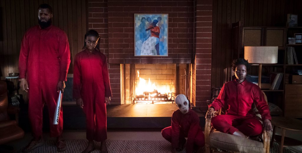 Still from "Us" featuring a creepy family in red jumpsuits in front of a fireplace