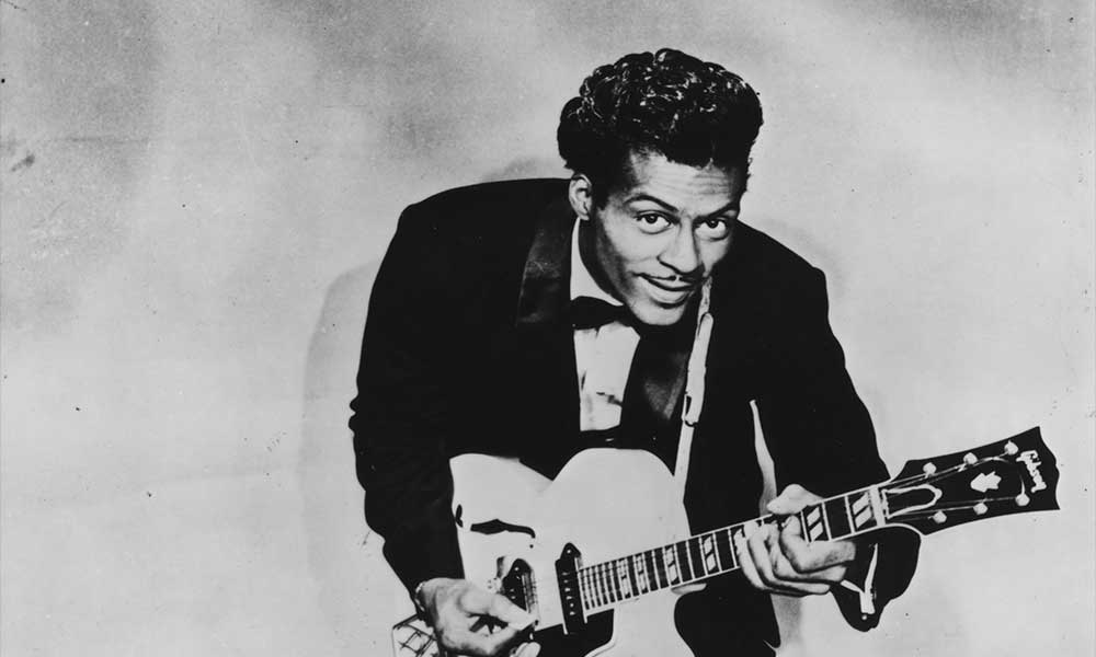 Black & white photo of Chuck Berry playing guitar and looking into the camera