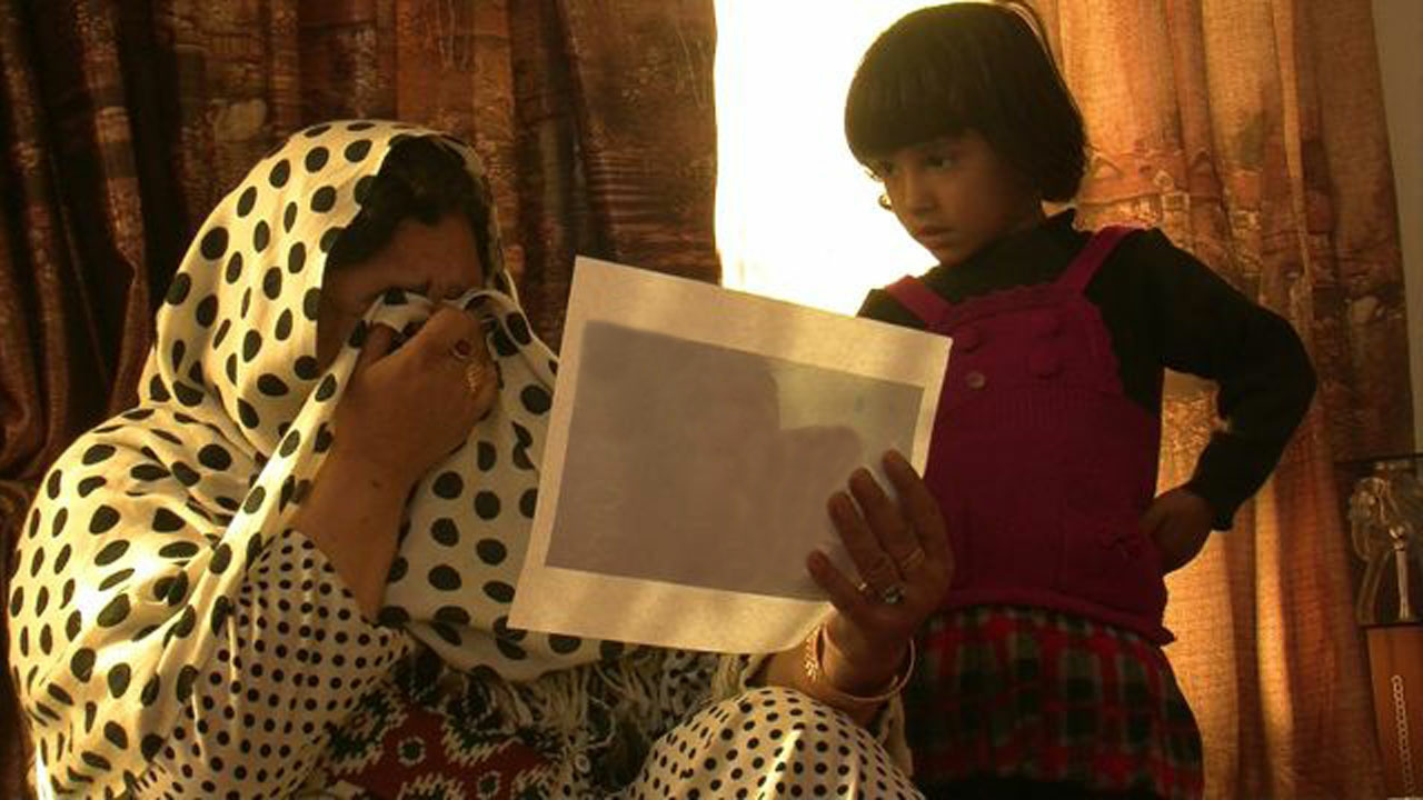 An Afghan woman wipes her tears with her hijab while looking at a photo