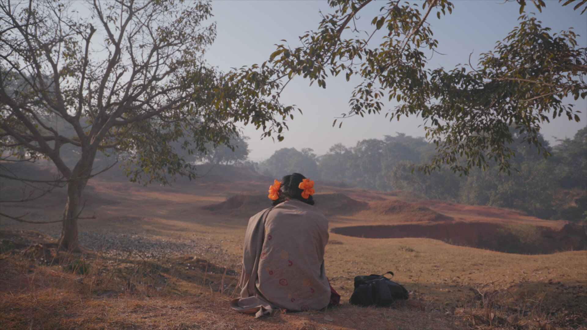 A girl seated on the ground facing away from the camera wrapped in a blanket