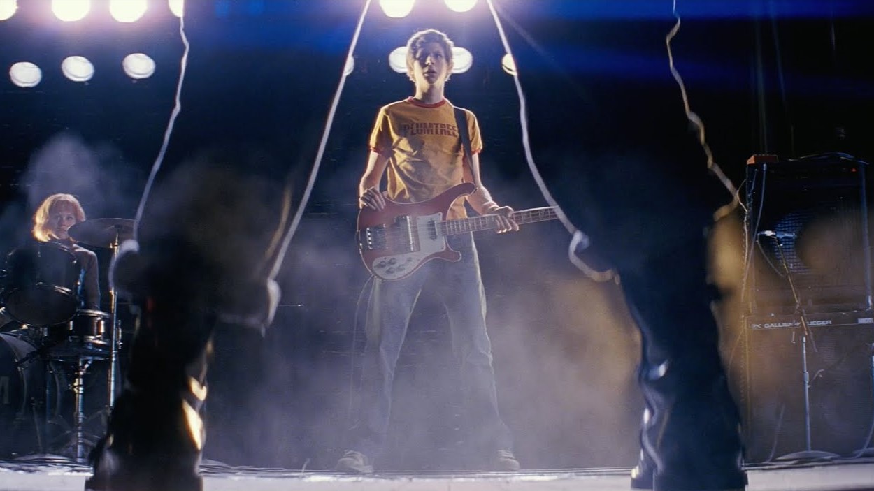 Still from "Scott Pilgrim vs. The World" featuring Scott holding a guitar in the background framed by a pair of legs in the foreground