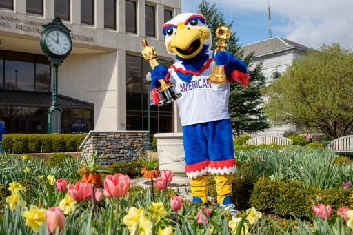 American University Mascot "Clawed Z. Eagle" standing in front of Bender Library holding an Academy Award and a Golden Globe