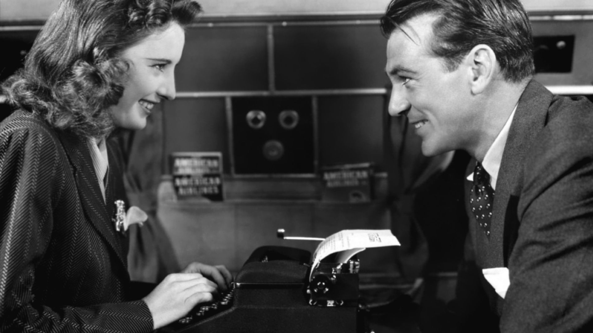 A man looks over at a woman using a typewriter.