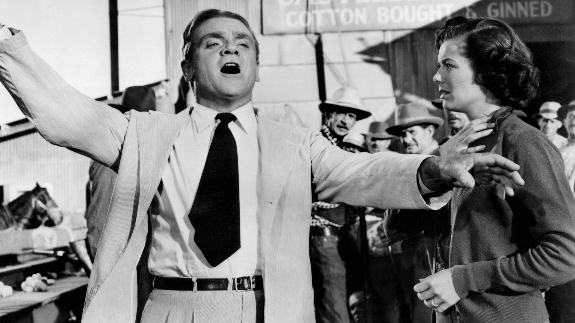A man in a suit gestures dramatically, while a woman looks on at him, concerned.