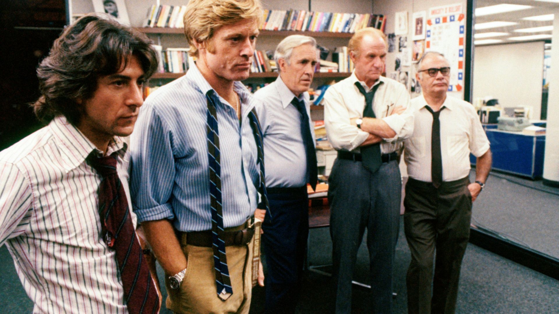 A group of 5 disheveled men in an office look at a subject beyond the shot.