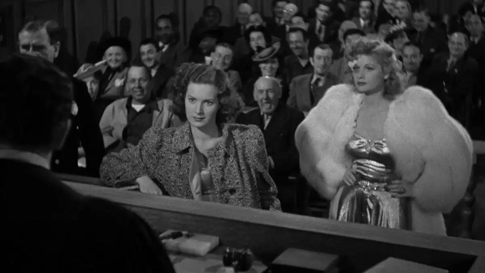 Two women stand at the front of a crowded court room.