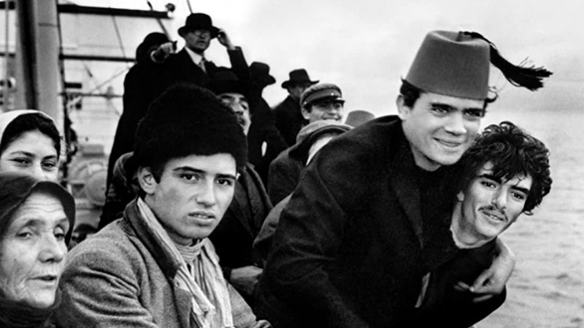 A group of people on the edge of the deck of a passenger boat look towards the camera.