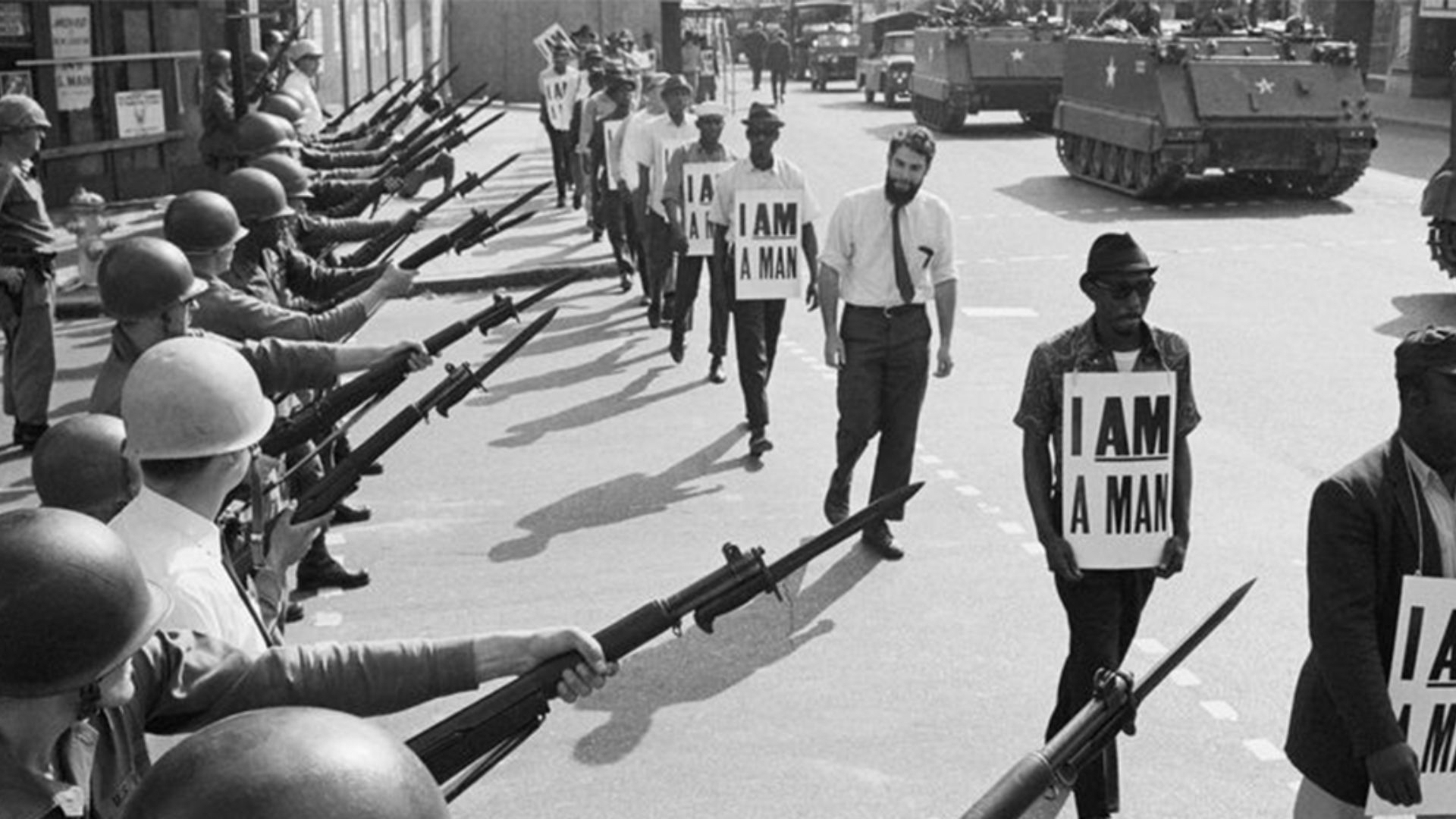 Armed military face "I AM A MAN" protesters in a tense civil rights confrontation.