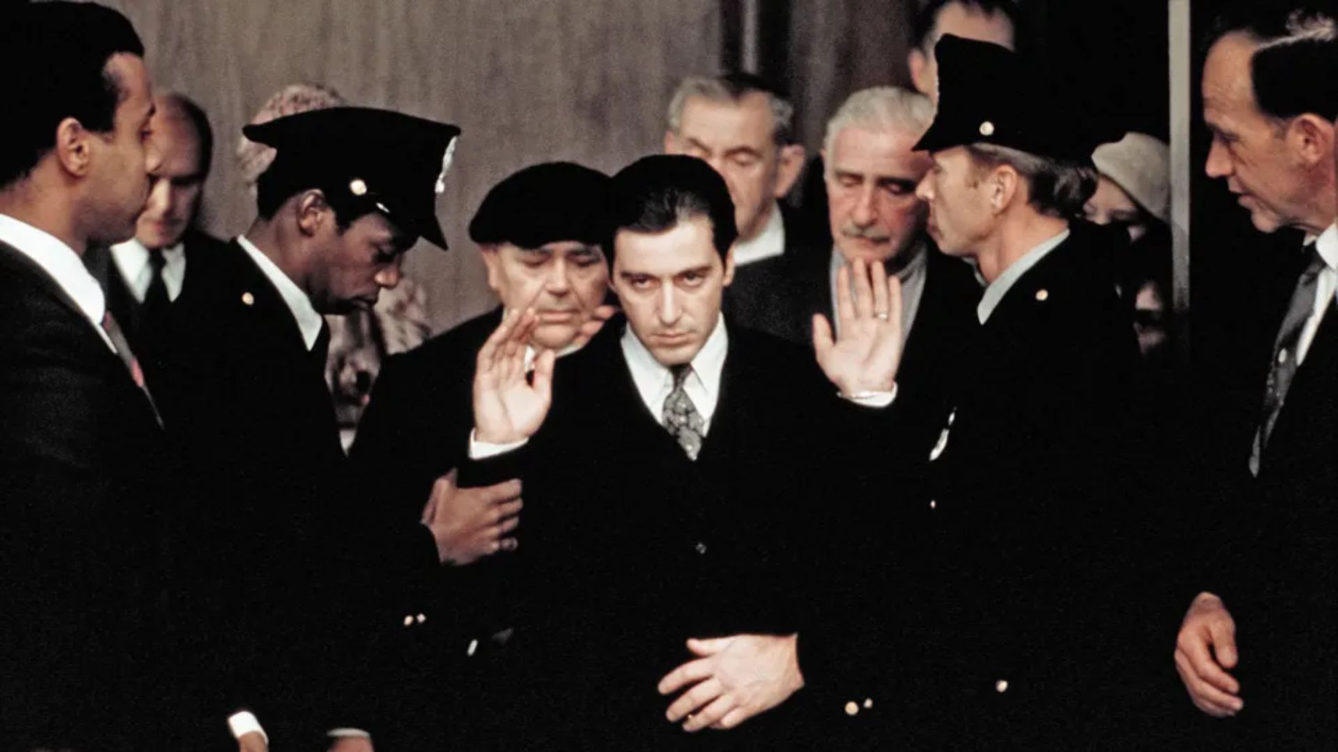 A man in a suit walks through a crowd of people dressed in police uniforms and black suits.