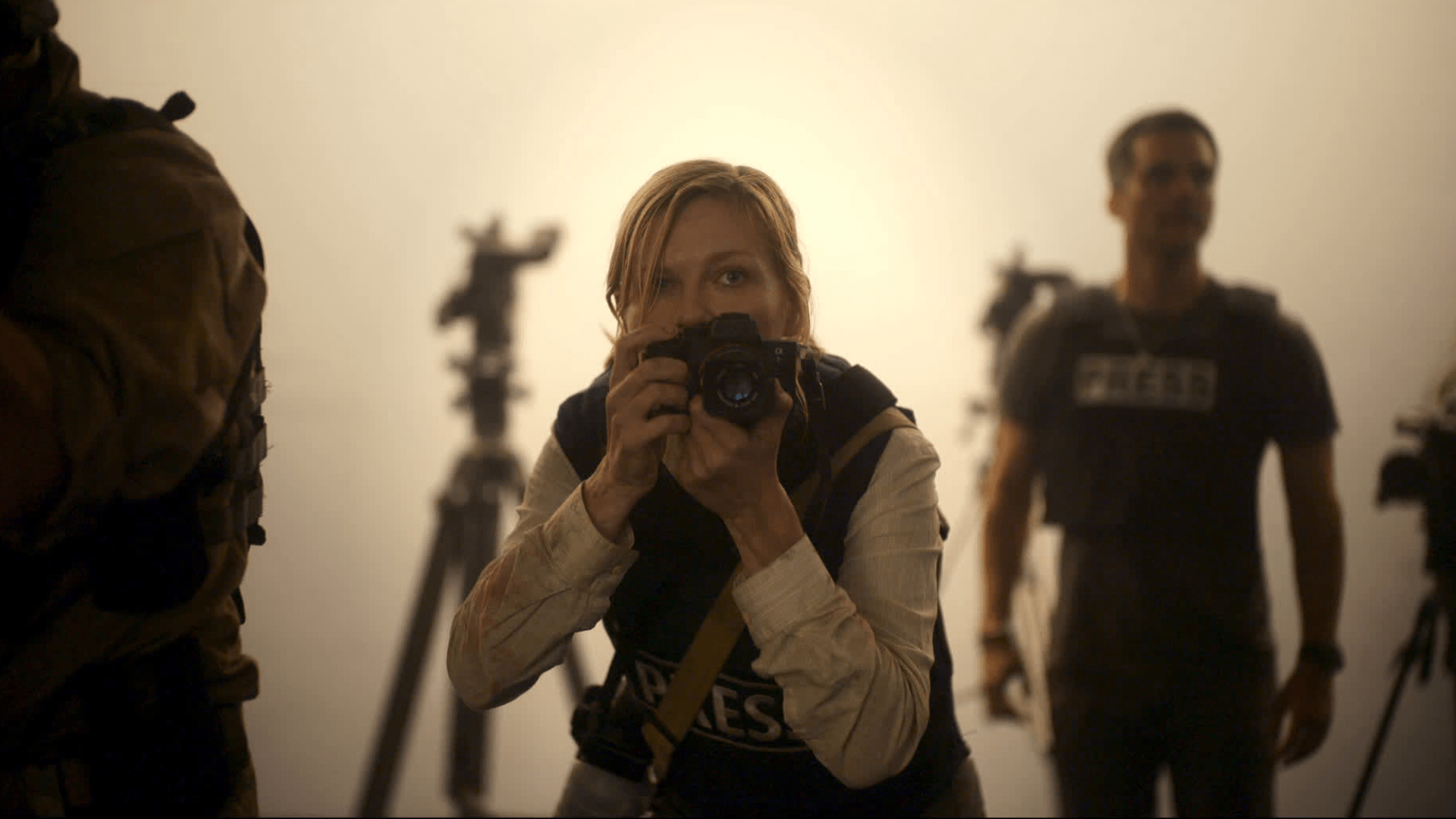 A woman poses with a camera in a dimly lit room with tripods in the background.