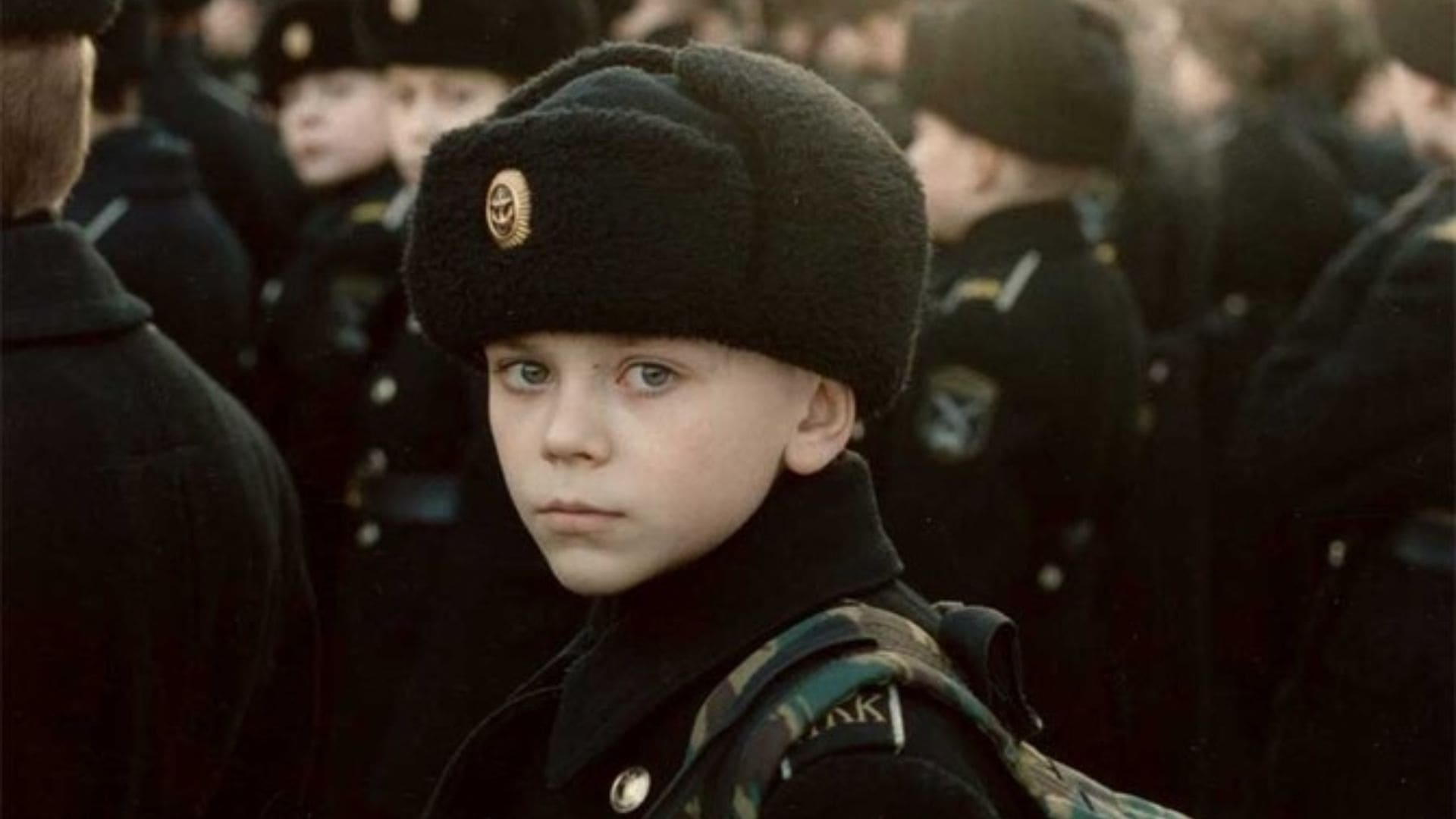A boy in a crowd of people looks towards the camera.
