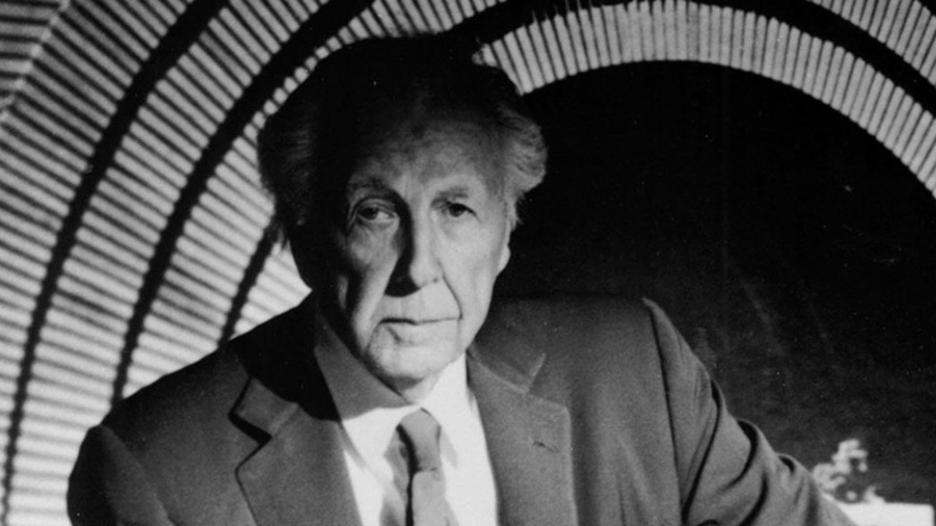 Architect Frank Lloyd Wright stands across an abstract backdrop.