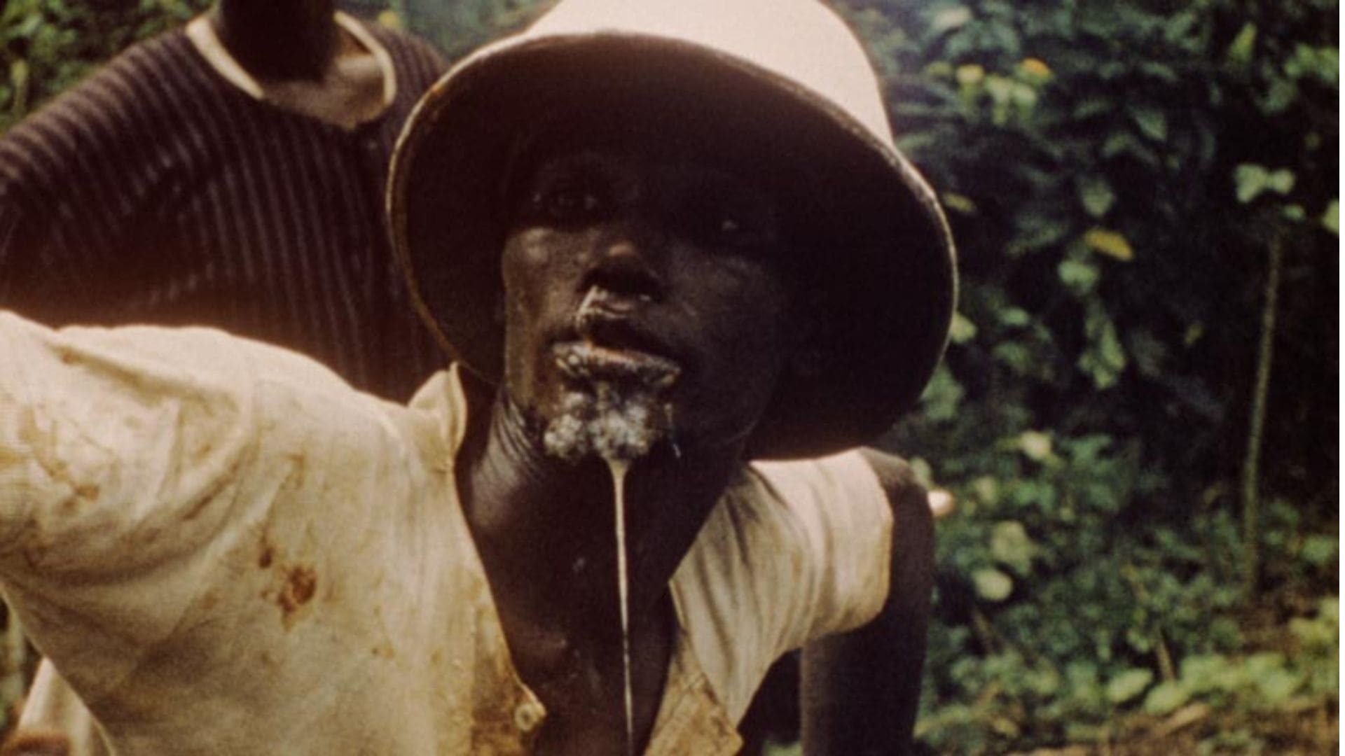 A liquid drips down the face of a man who is walking through a forest.