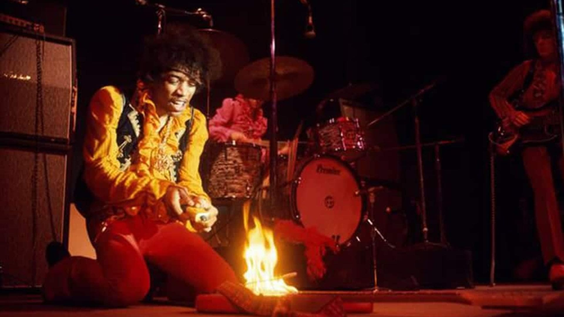 Musician Jimi Hendrix kneels in front of his guitar, which has been set ablaze.