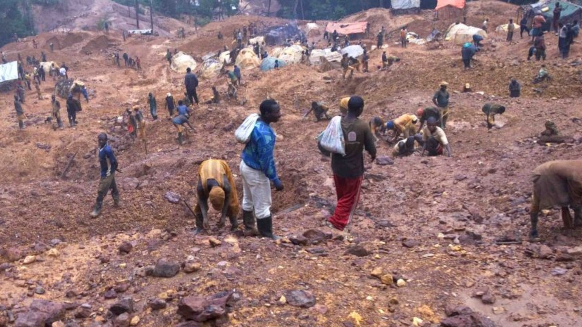 A desolate mountainside is mined and picked at by people scattered over it.