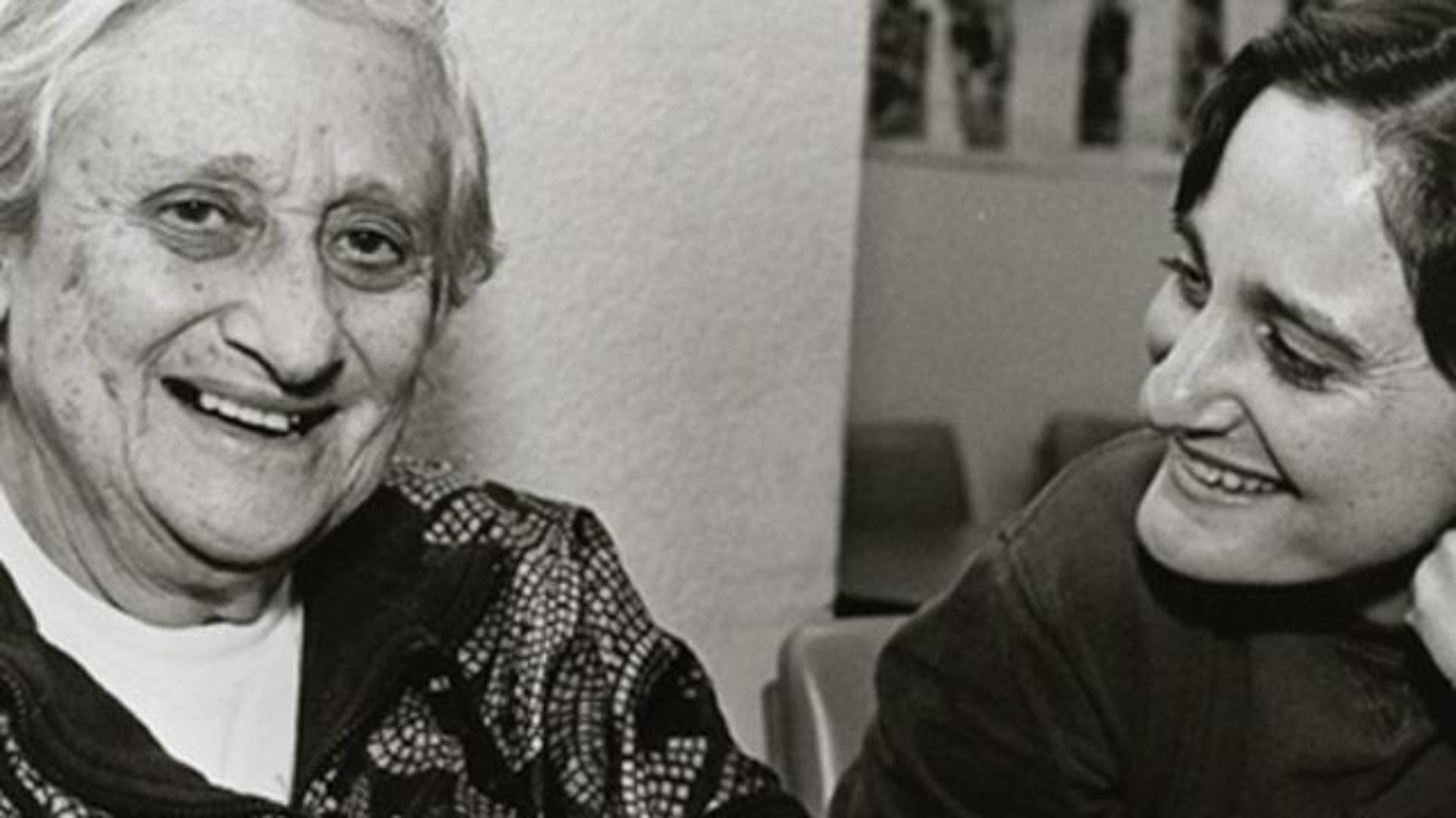 An older woman on the left smiles, while her daughter gazes at her on the right side of the image.