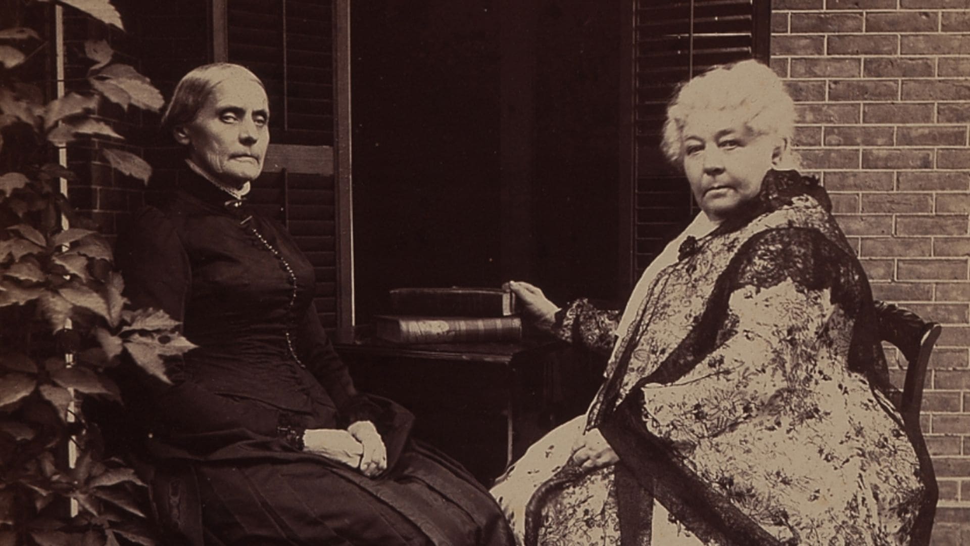 Two women in early 19th-century apparel gaze towards the camera.