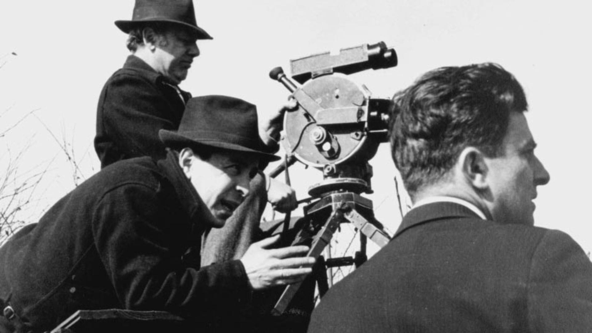 A man operates a camera while two men to the left of him look onward.
