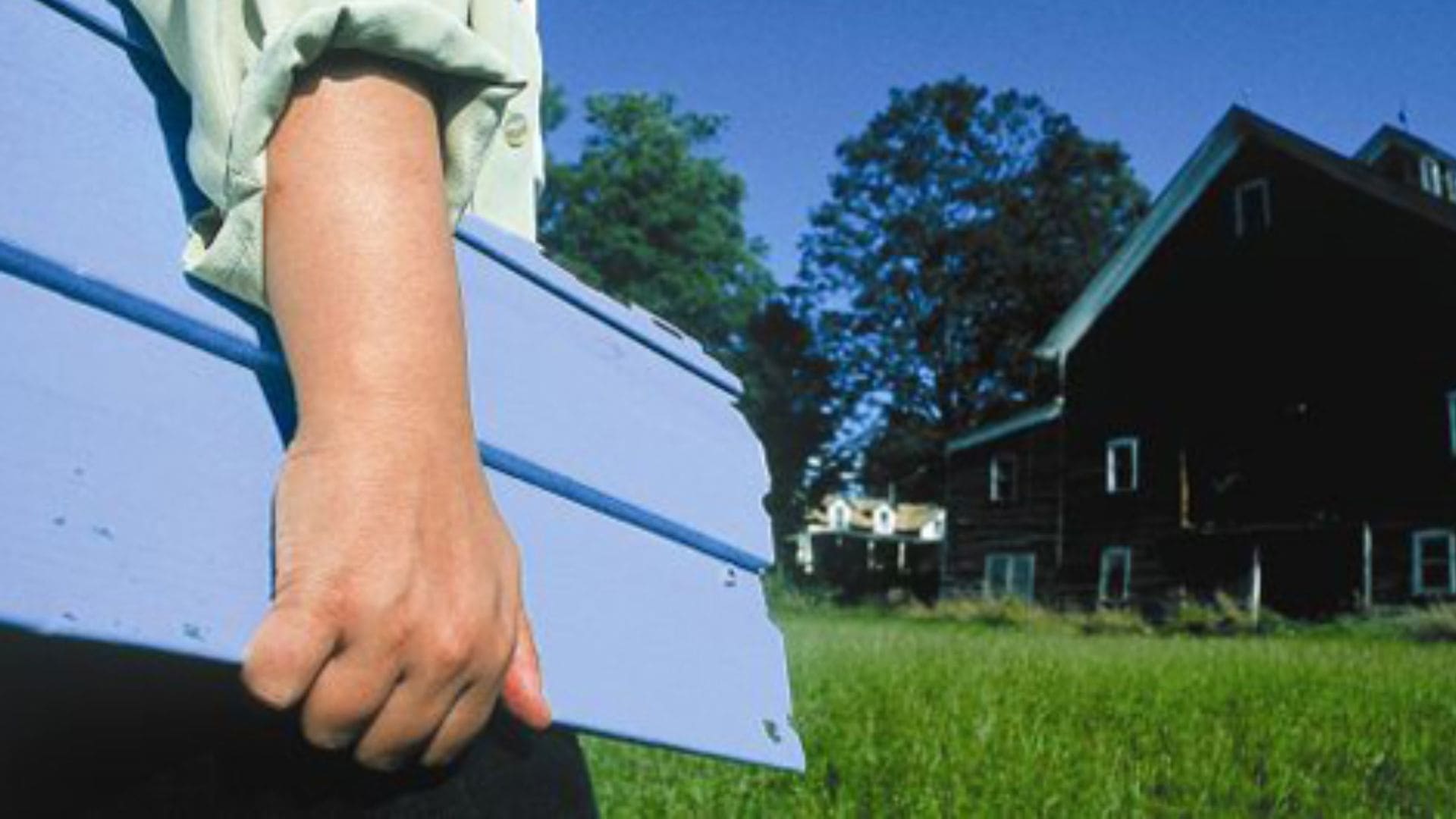 A low shot of an arm holding a blue panel, with a two-story home in front of the figure.