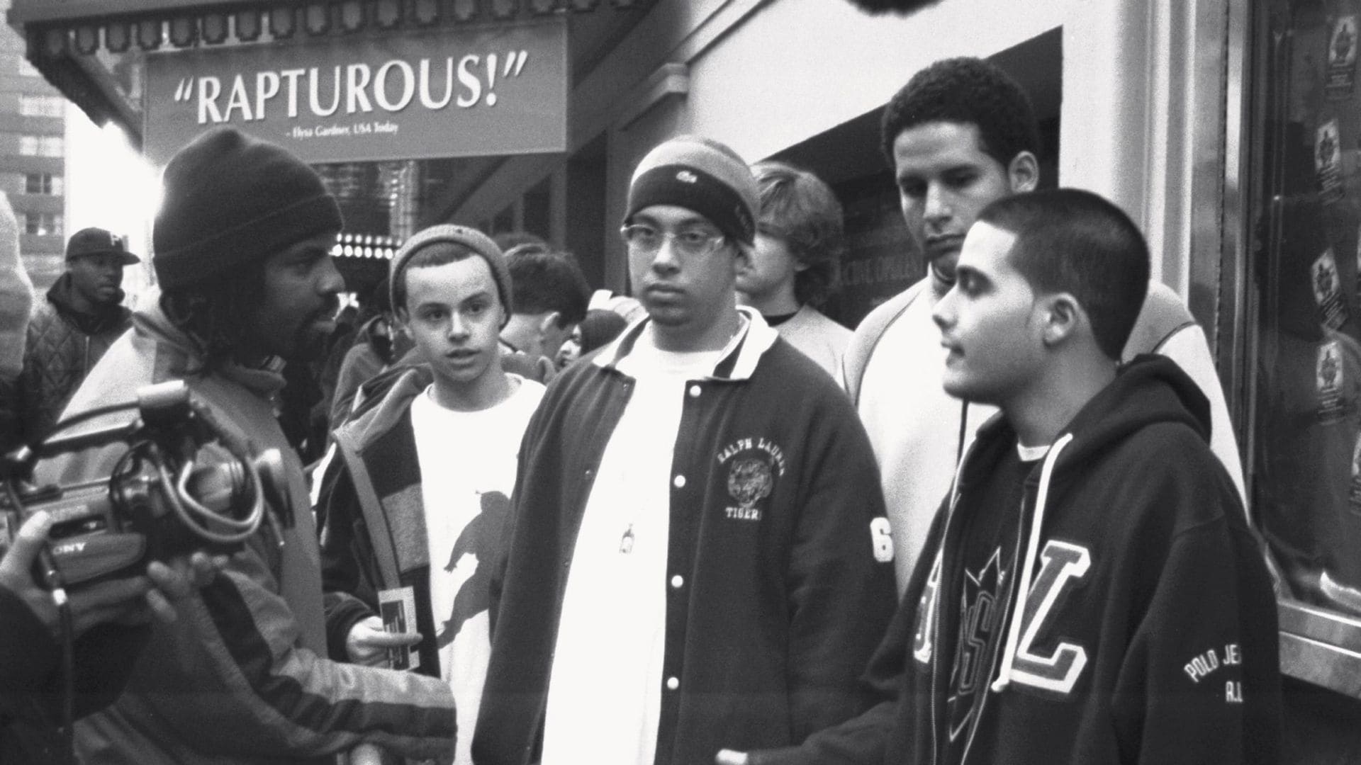 A group of young men stand in front of a movie theatre.