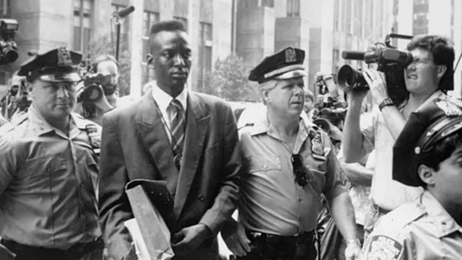 A man is escorted by two police officers, while he is being photographed in a crowd.