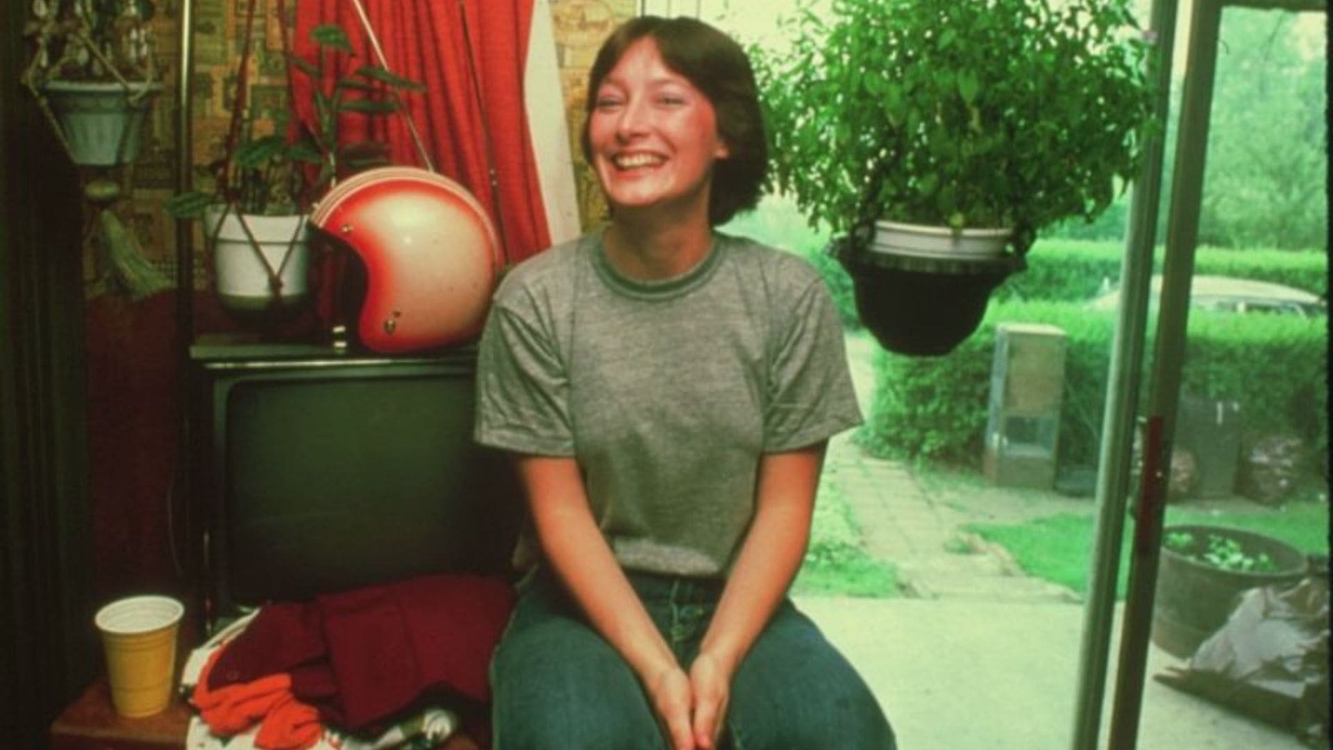 A young girl in casual dress sits smiling in front of a TV set.