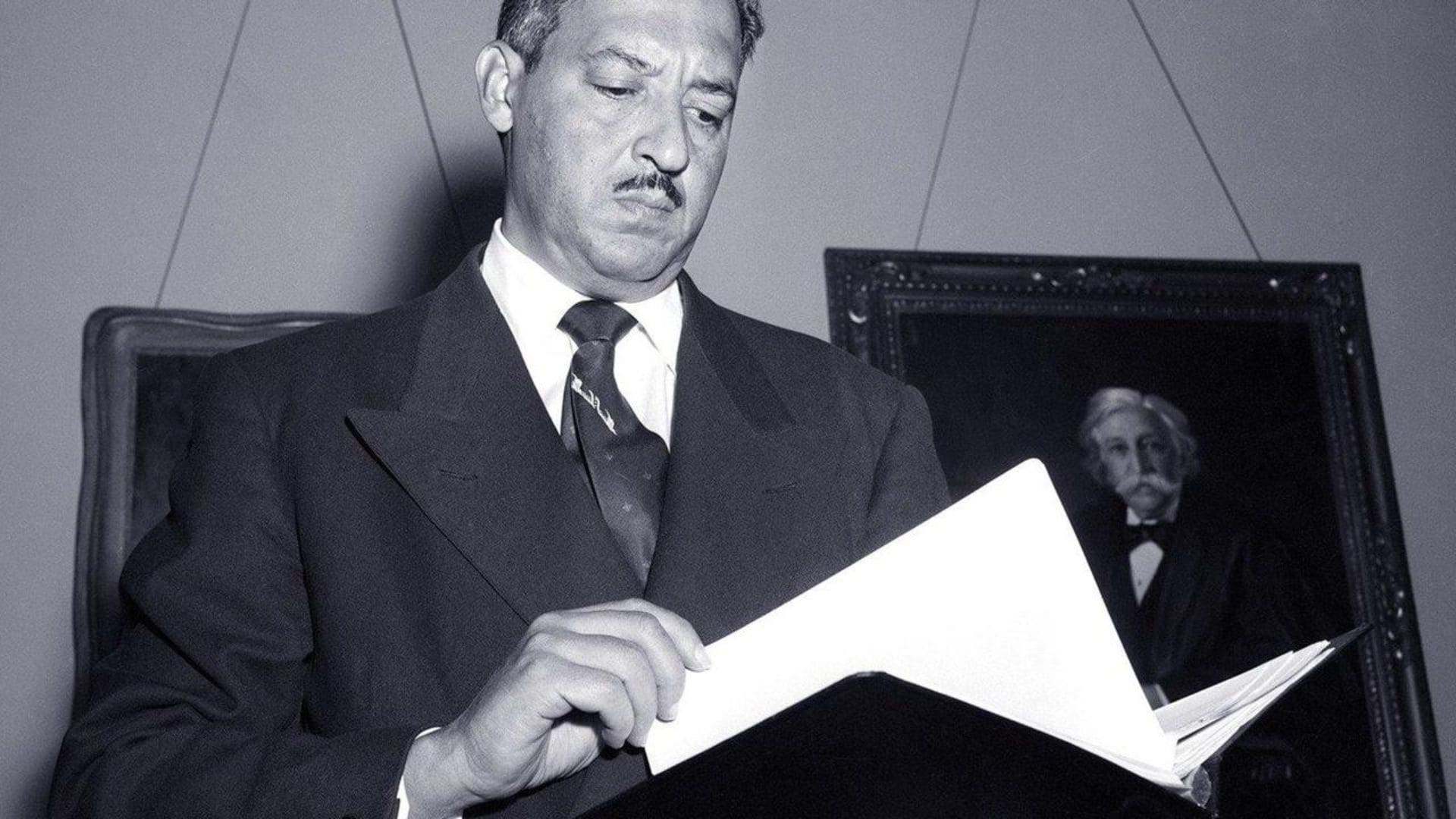 A man in a suit looks through a large book.