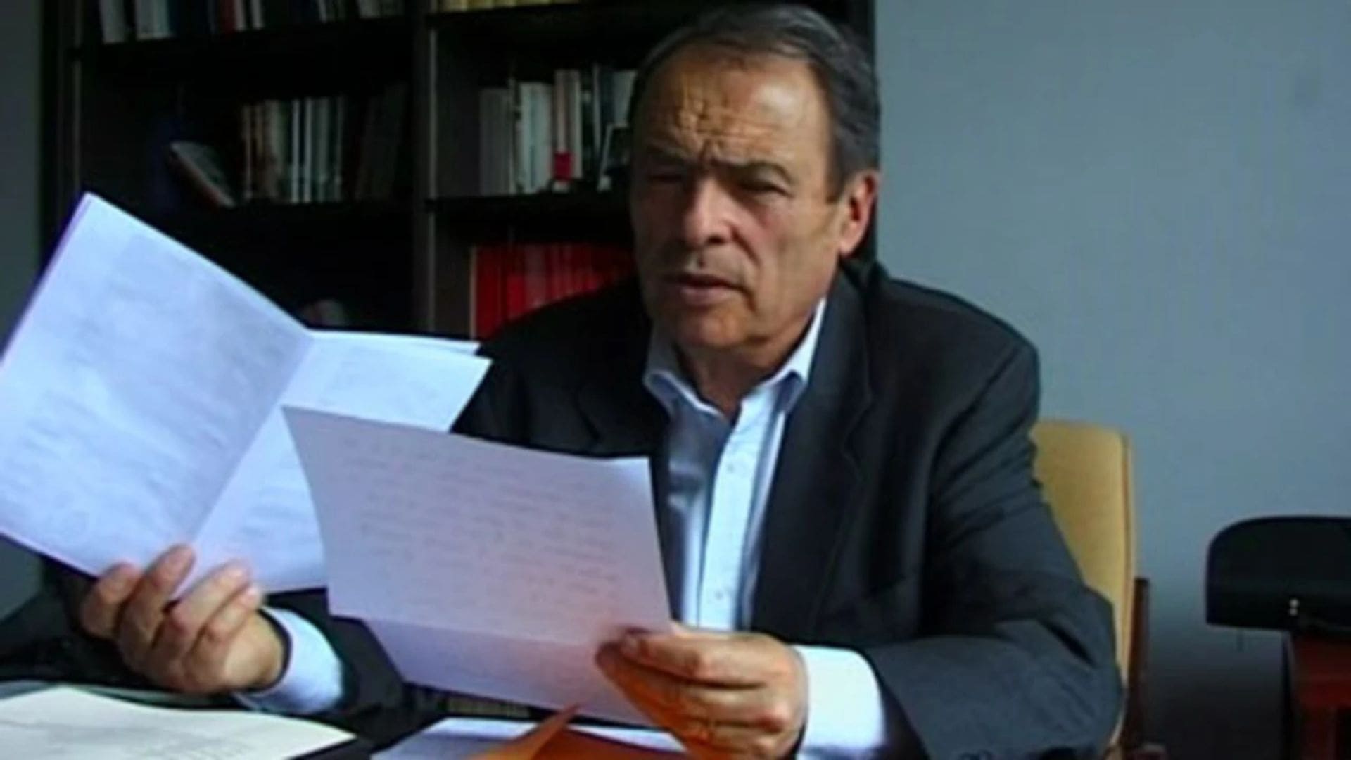A man holds several papers in both of his hands, while sitting at his desk.