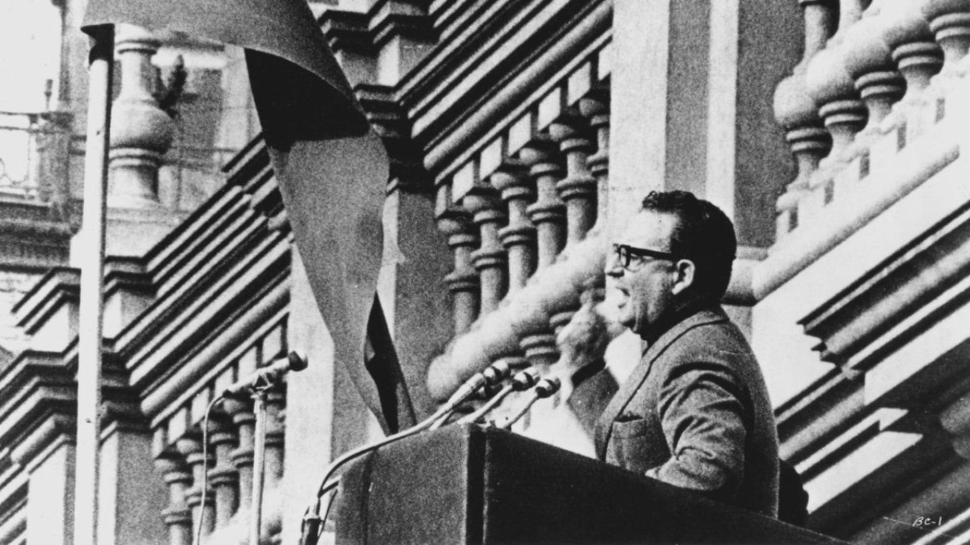 A man stands behind a podium, speaking and motioning.