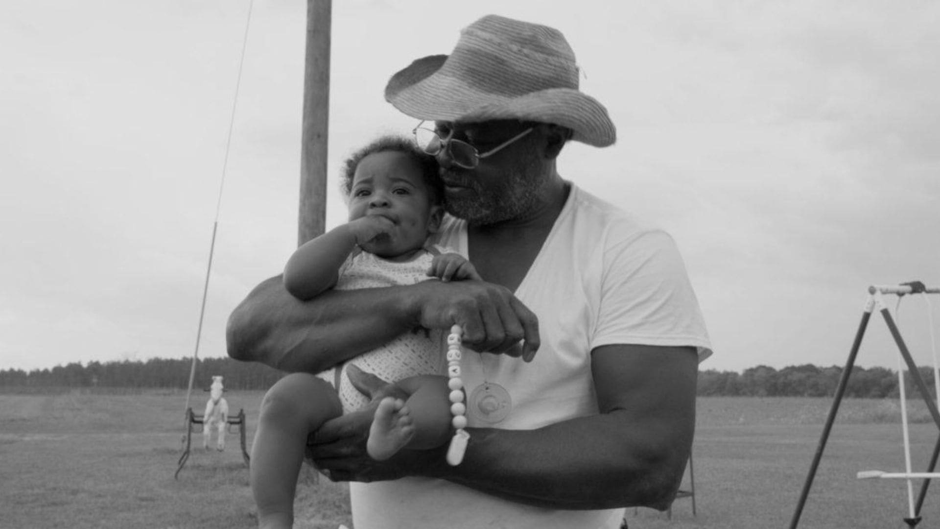 A man holds a baby in a field.
