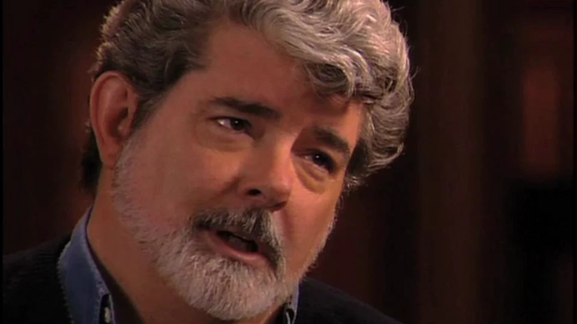 Director George Lucas caught mid-sentence in front of a solid backdrop.