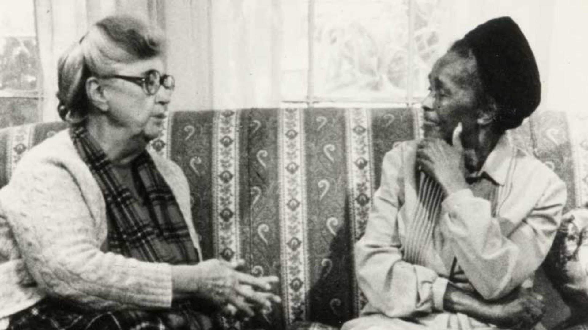 Two older women are in discussion with each other, sitting on a couch.