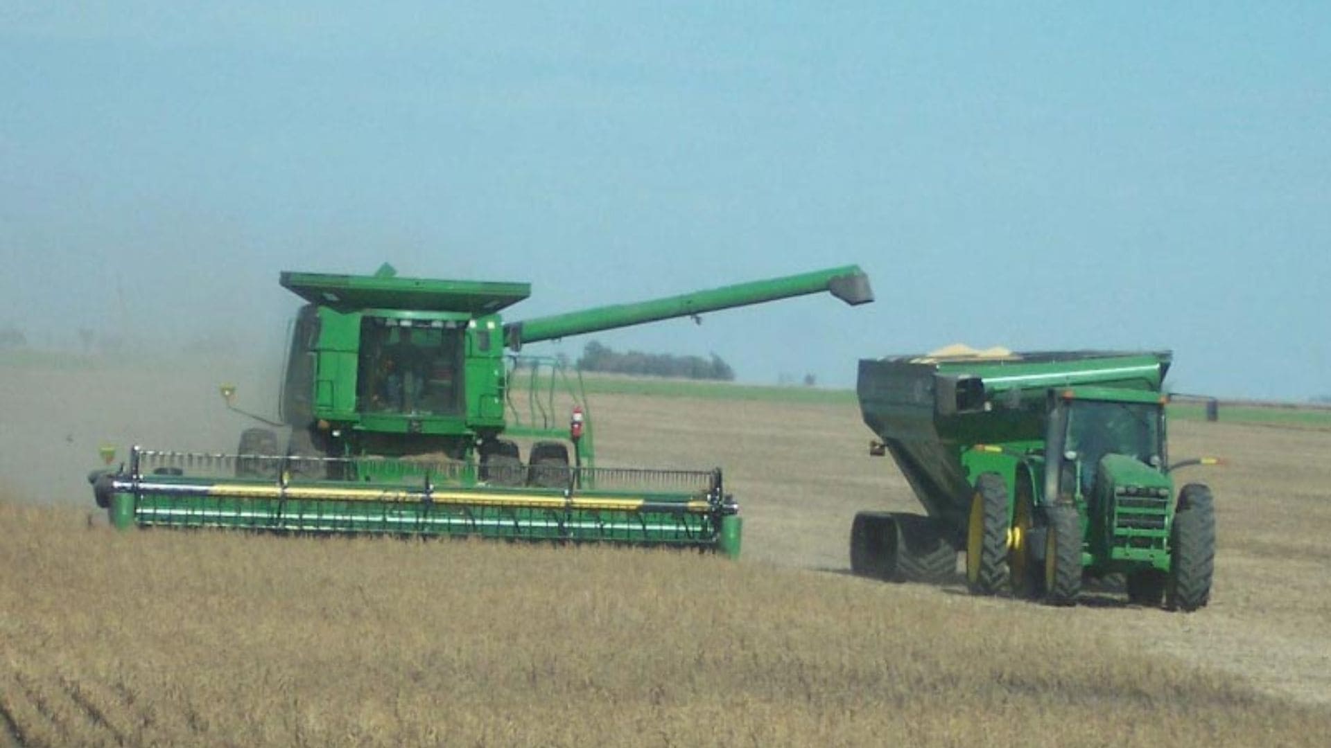 A harvester and tractor harvesting a crop in a field.