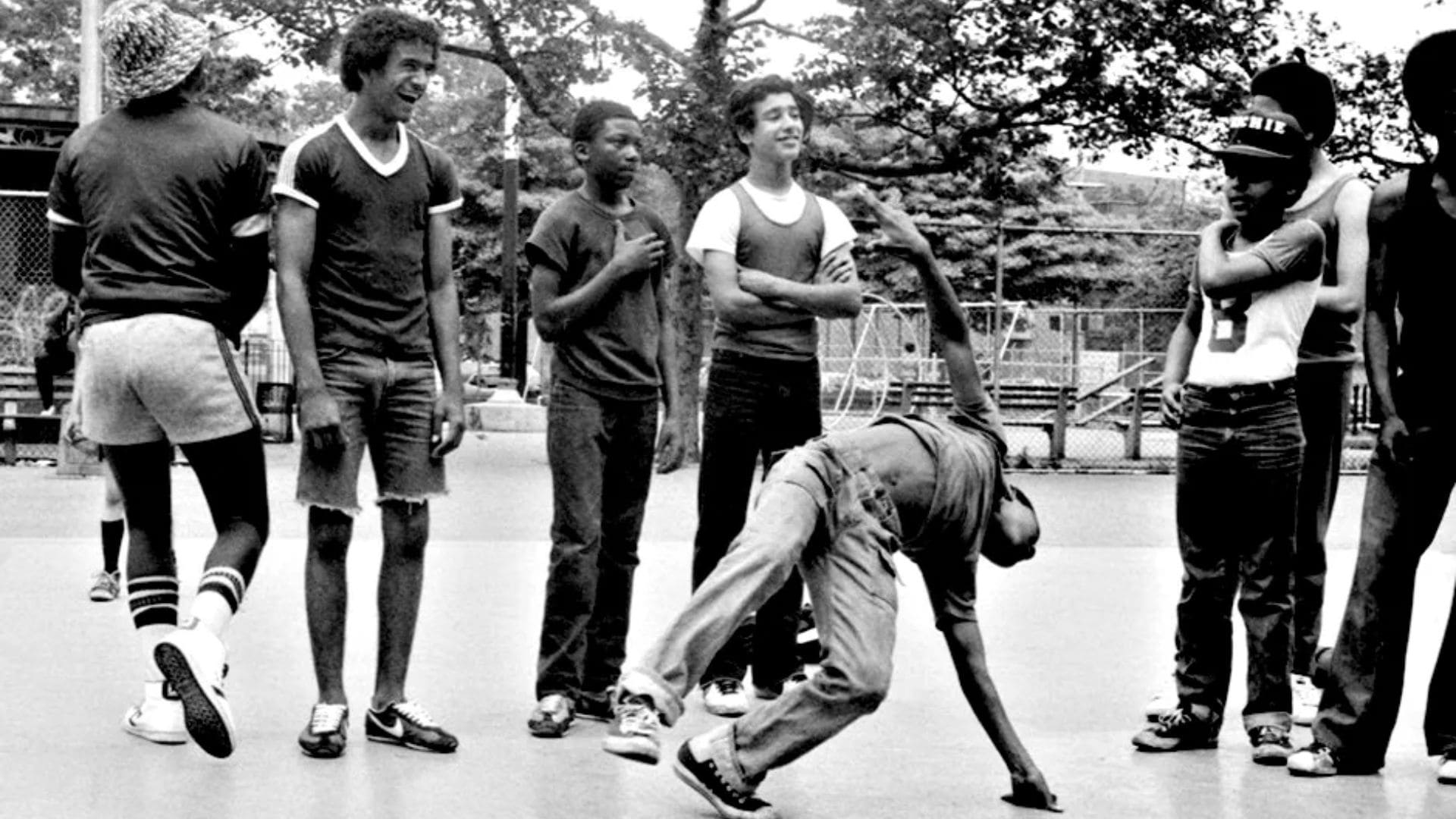 A group of people at a park watch a young man breakdance.