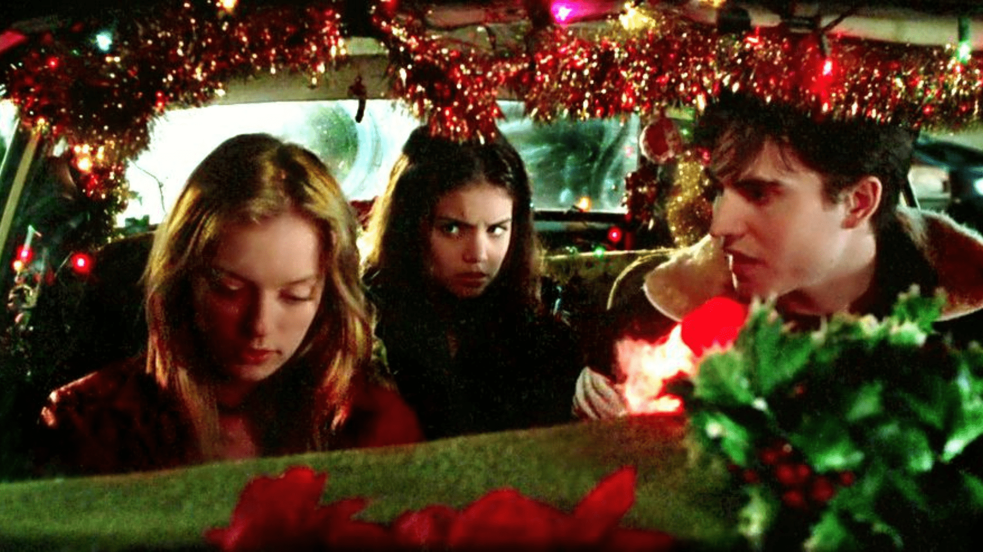A man and a woman sit in the front of a decorated car, with another woman in the backseat.