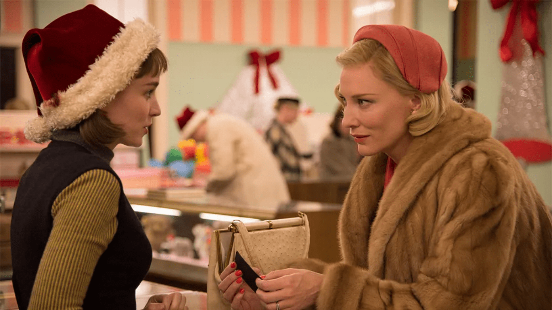 A young woman with a Santa hat stands across a store counter from an older woman dressed in a fur coat.