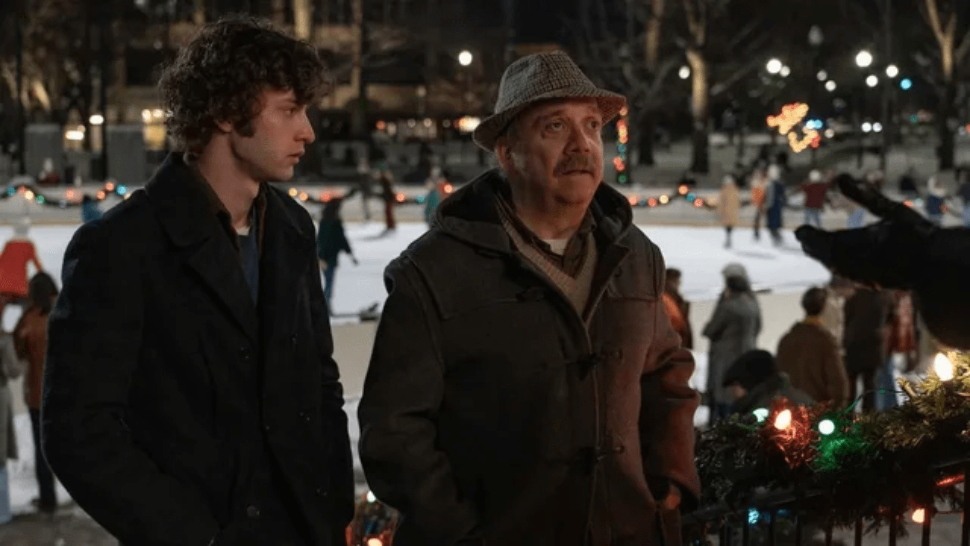 A young man and an older one stand side by side in front of an ice skating rink.
