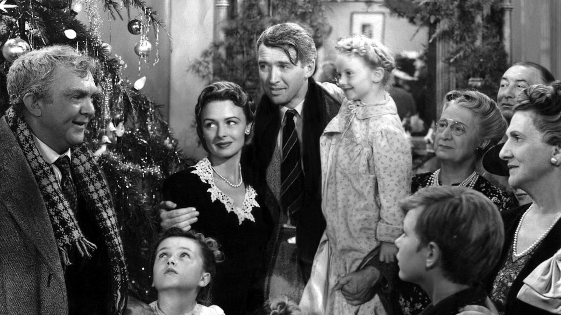 A black-and-white photograph of a group of people crowding around a Christmas tree.