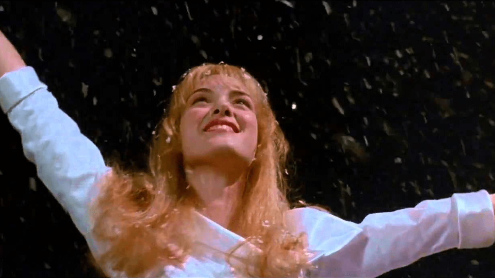 A young woman holds her arms up to falling snow.