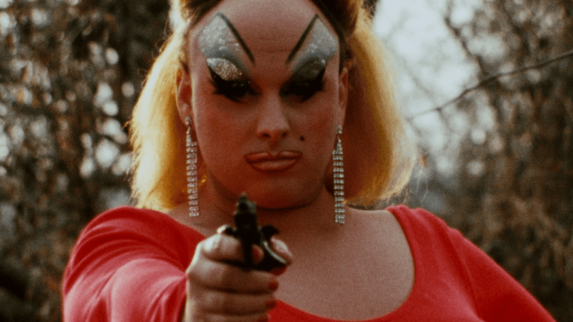 A woman with heavy makeup holds a gun at the camera.